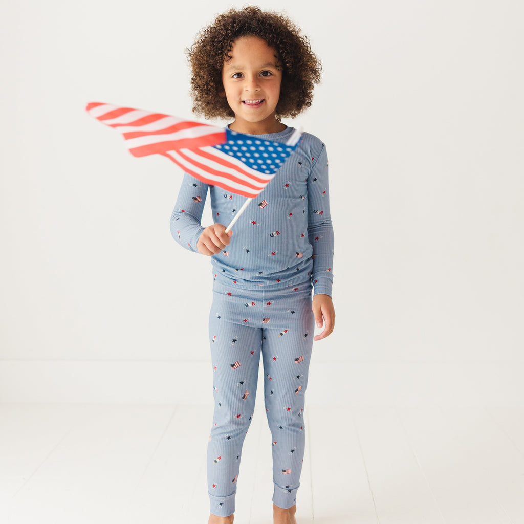 Child wearing a blue pajama set with stars and flag patterns, holding an American flag on a white background