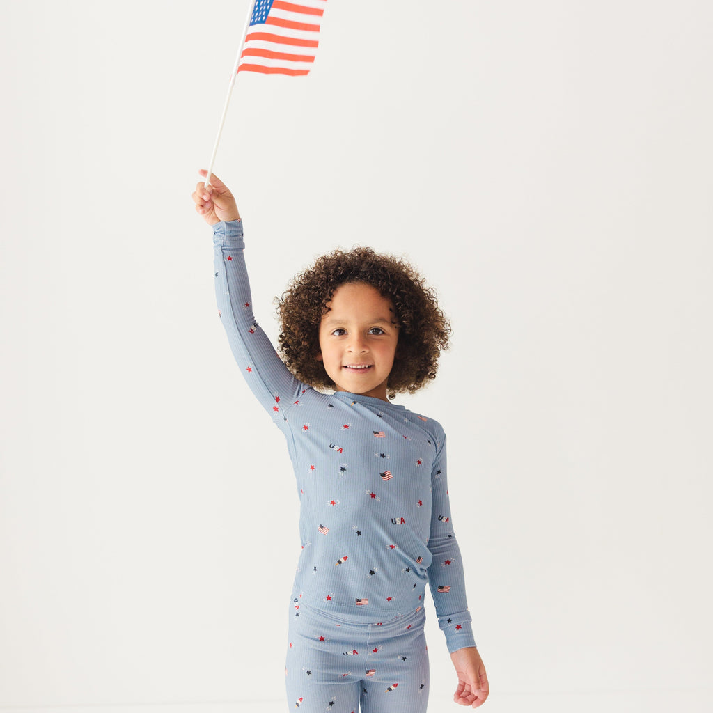 Child wearing a blue pajama set with stars and flag patterns, holding an American flag on a white background