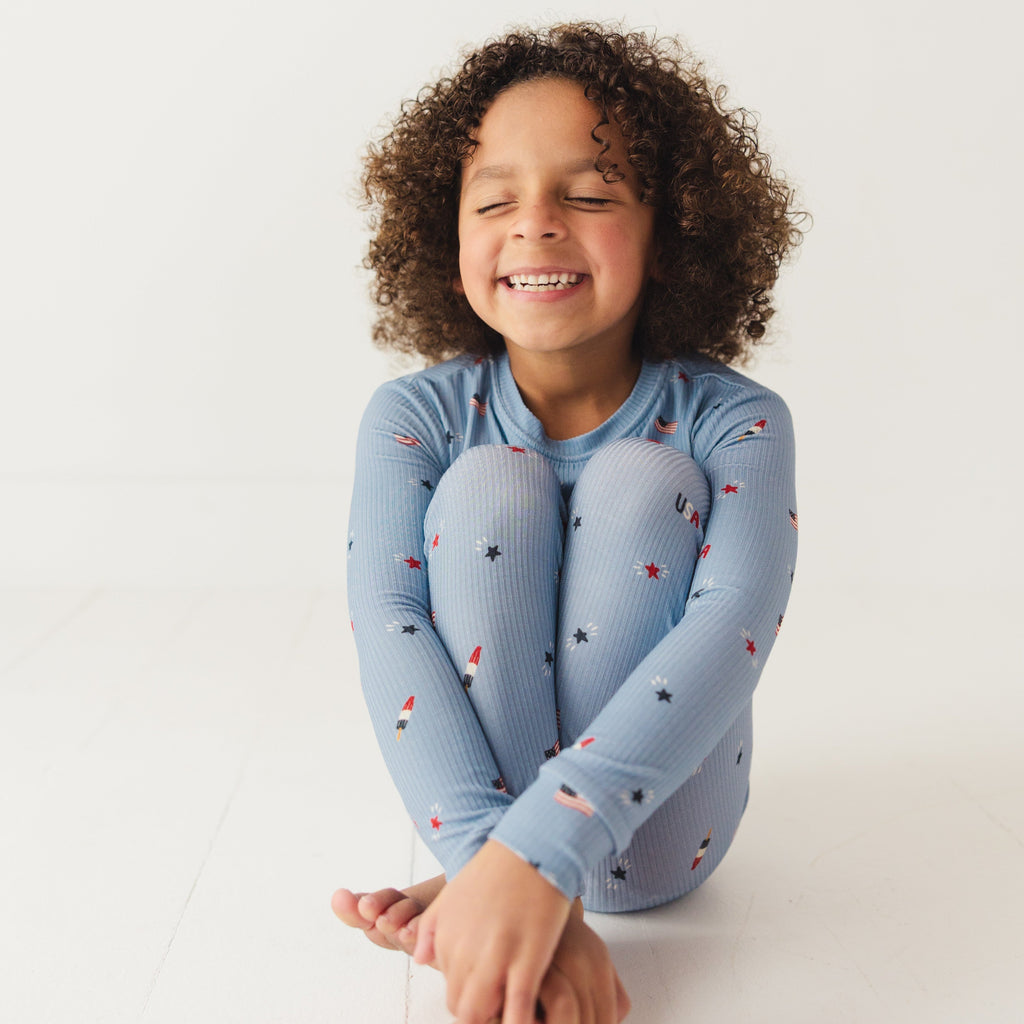 Child smiling while wearing a blue pajama set with stars and flag patterns on a white background