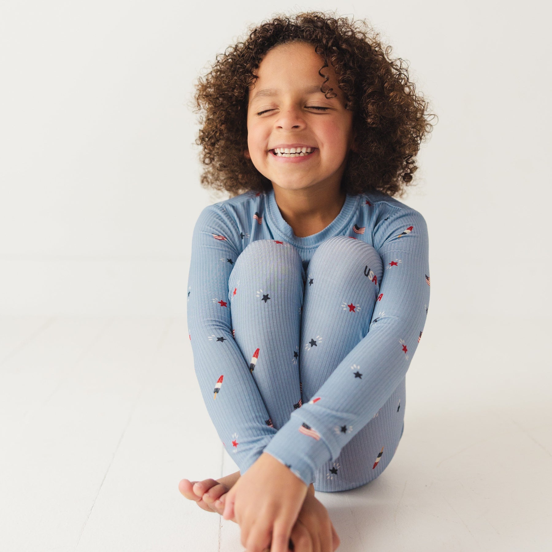 Child smiling while wearing a blue pajama set with stars and flag patterns on a white background