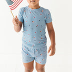 Child wearing a light blue outfit with small American flag pattern, holding a miniature American flag.