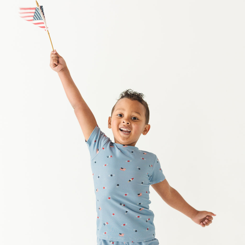 Child wearing a light blue outfit with small American flag pattern, holding a miniature American flag.