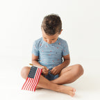 Child sitting on the floor wearing a light blue outfit with small American flag pattern, holding a miniature American flag.
