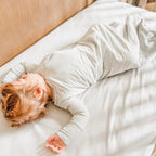 Child sleeping in a crib with white bedding, wearing a gray sleeping bag