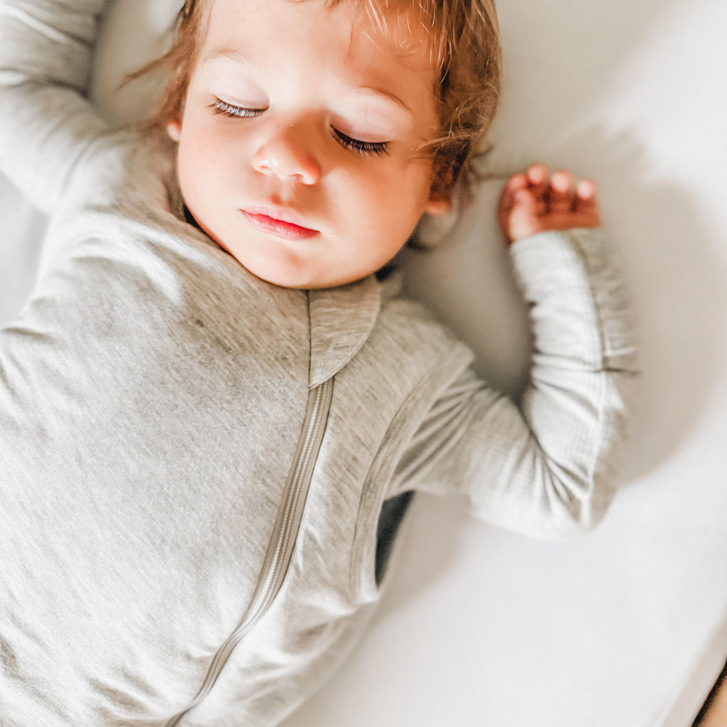 Close up of a child sleeping in a crib with white bedding, wearing a gray sleeping bag