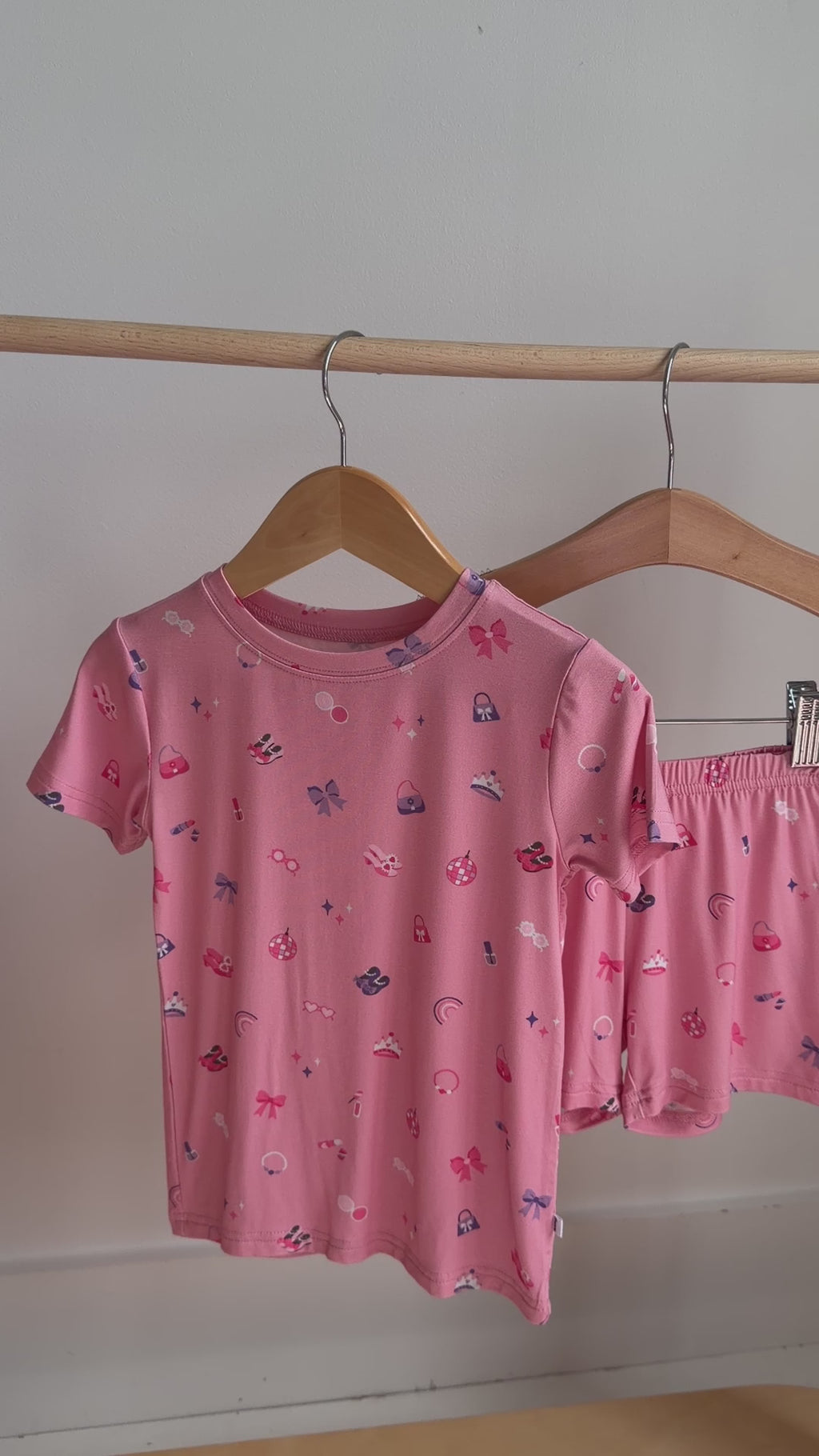 Video of a pink children's pajama shorts set with girly patterns hanging on a rack