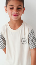 Child wearing a white t-shirt with checkered sleeves on a white background