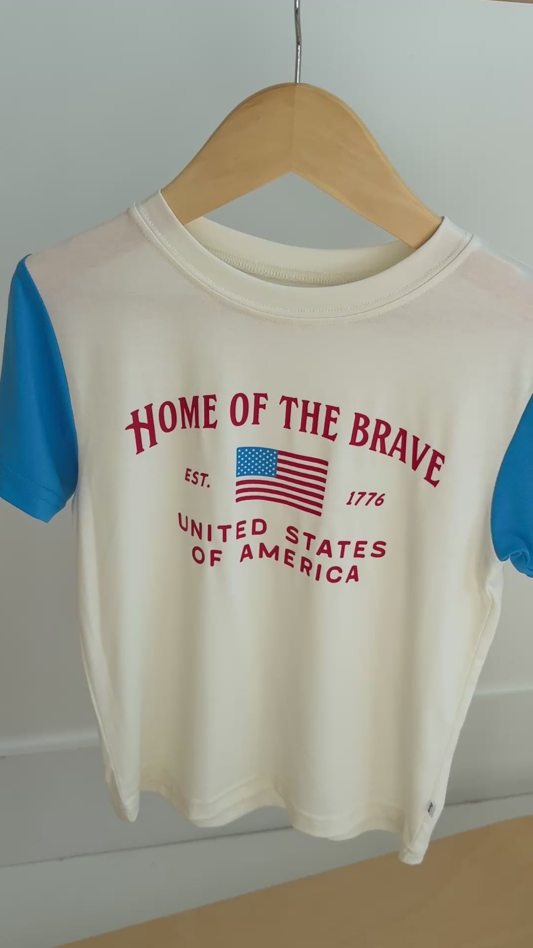 'Home of the Brave' t-shirt with blue sleeves hanging on a rack