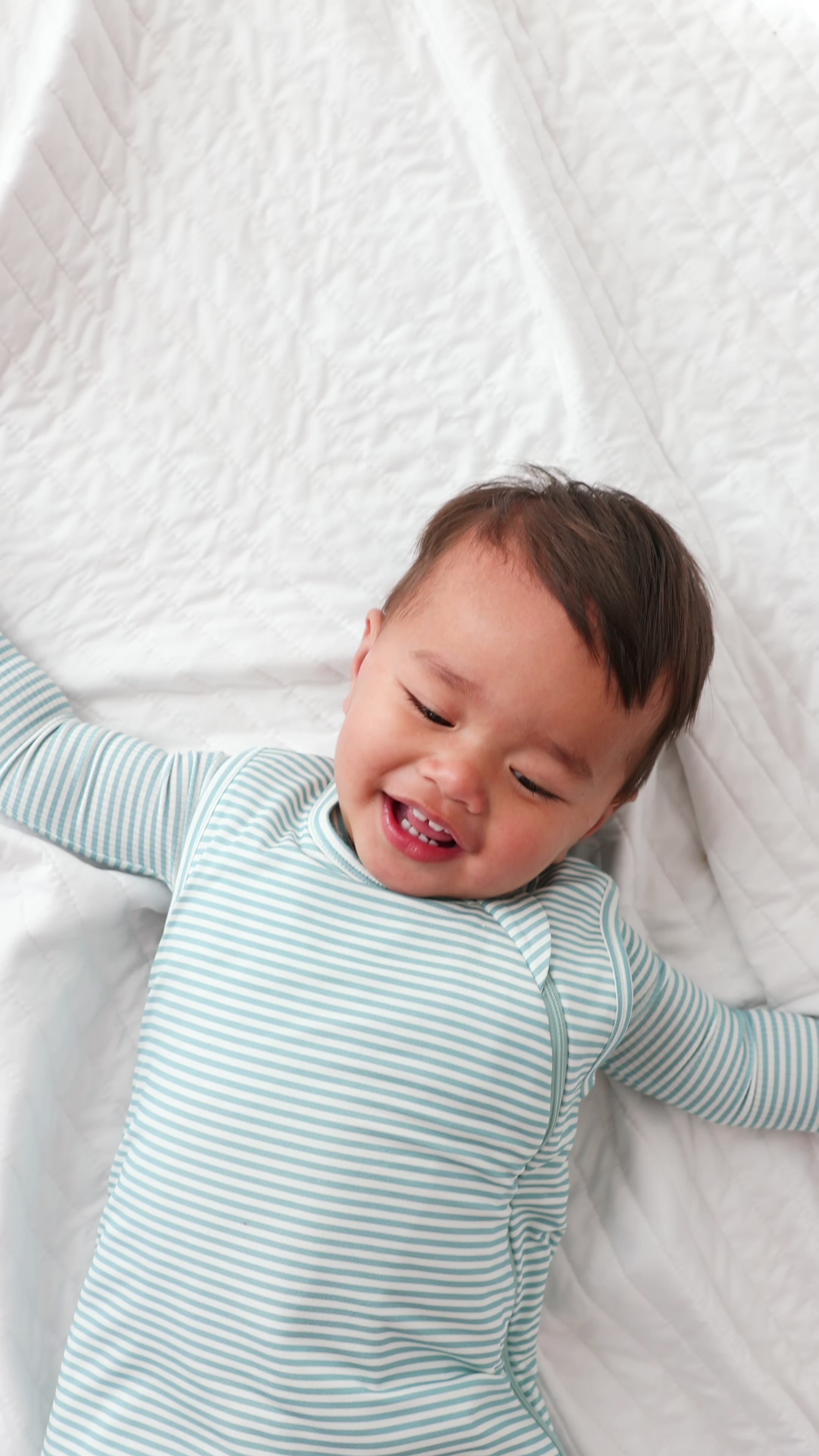 Video of a baby wearing a light blue striped onesie and sleep sack on a white background