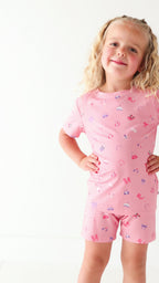 Video of a child wearing a pink shorts pajama set with heart sunglasses on a white background