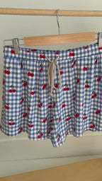 Video of a blue checkered pajama shorts with cherry pattern hanging on a rack
