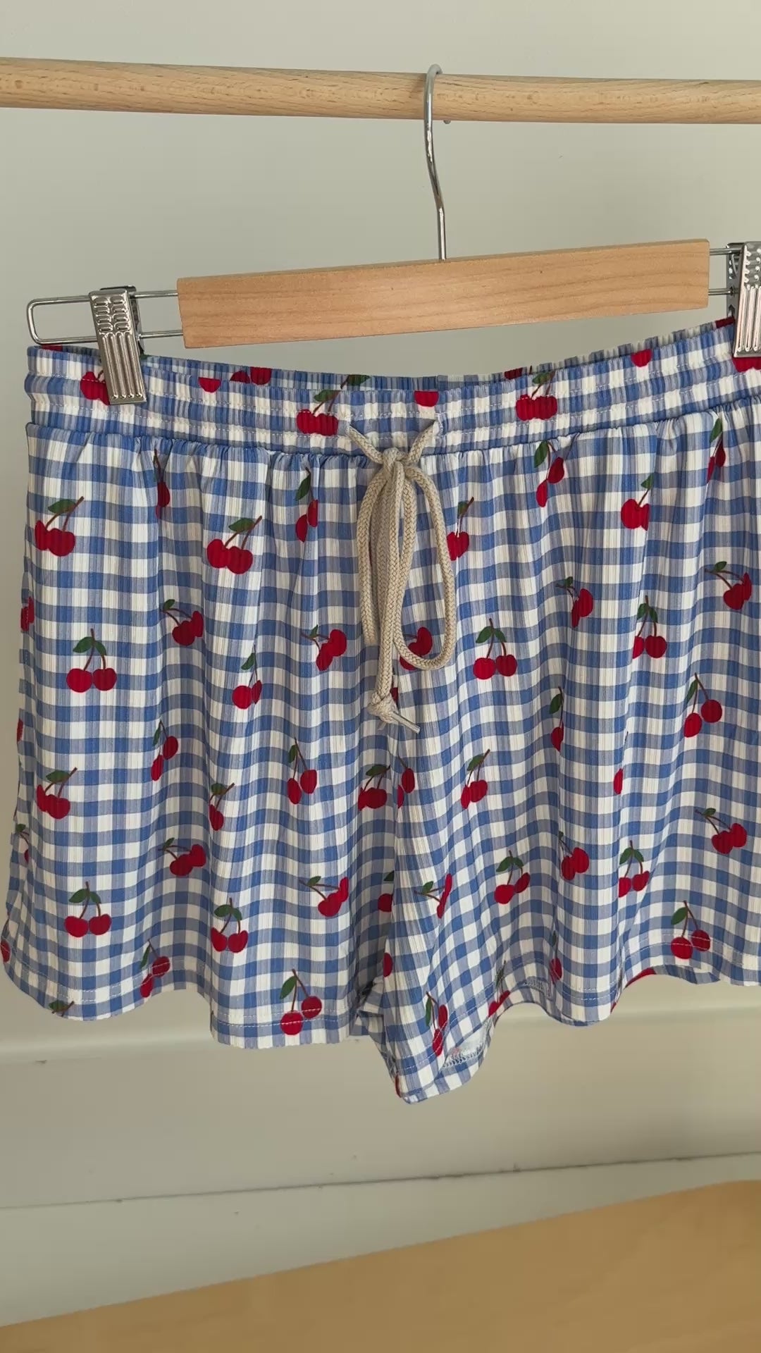 Video of a blue checkered pajama shorts with cherry pattern hanging on a rack