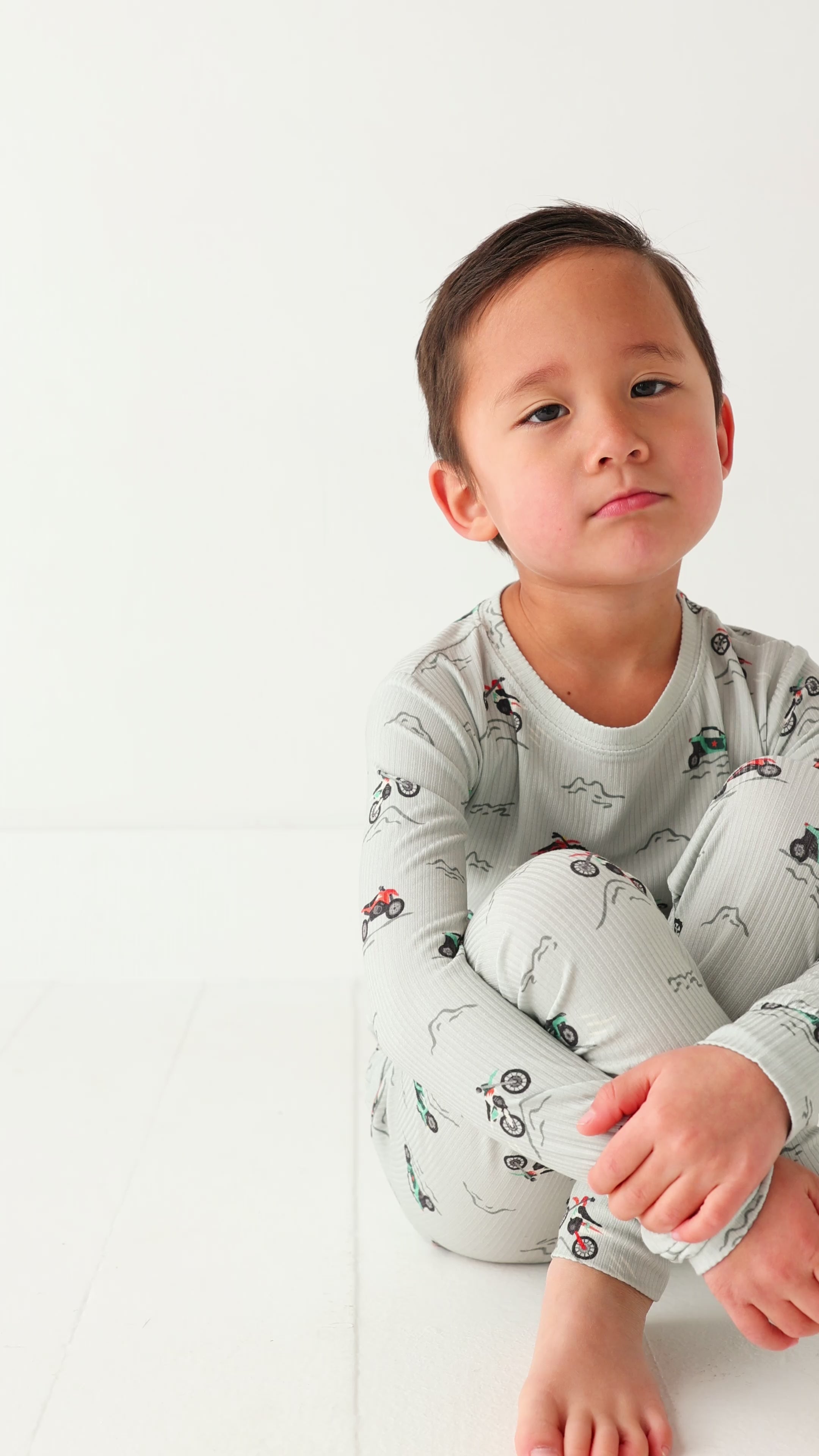 Child wearing a long sleeve pajama set with vehicle patterns on a white background