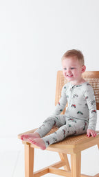 Child wearing a long-sleeve onesie with vehicle patterns sitting on a wooden chair against a white background