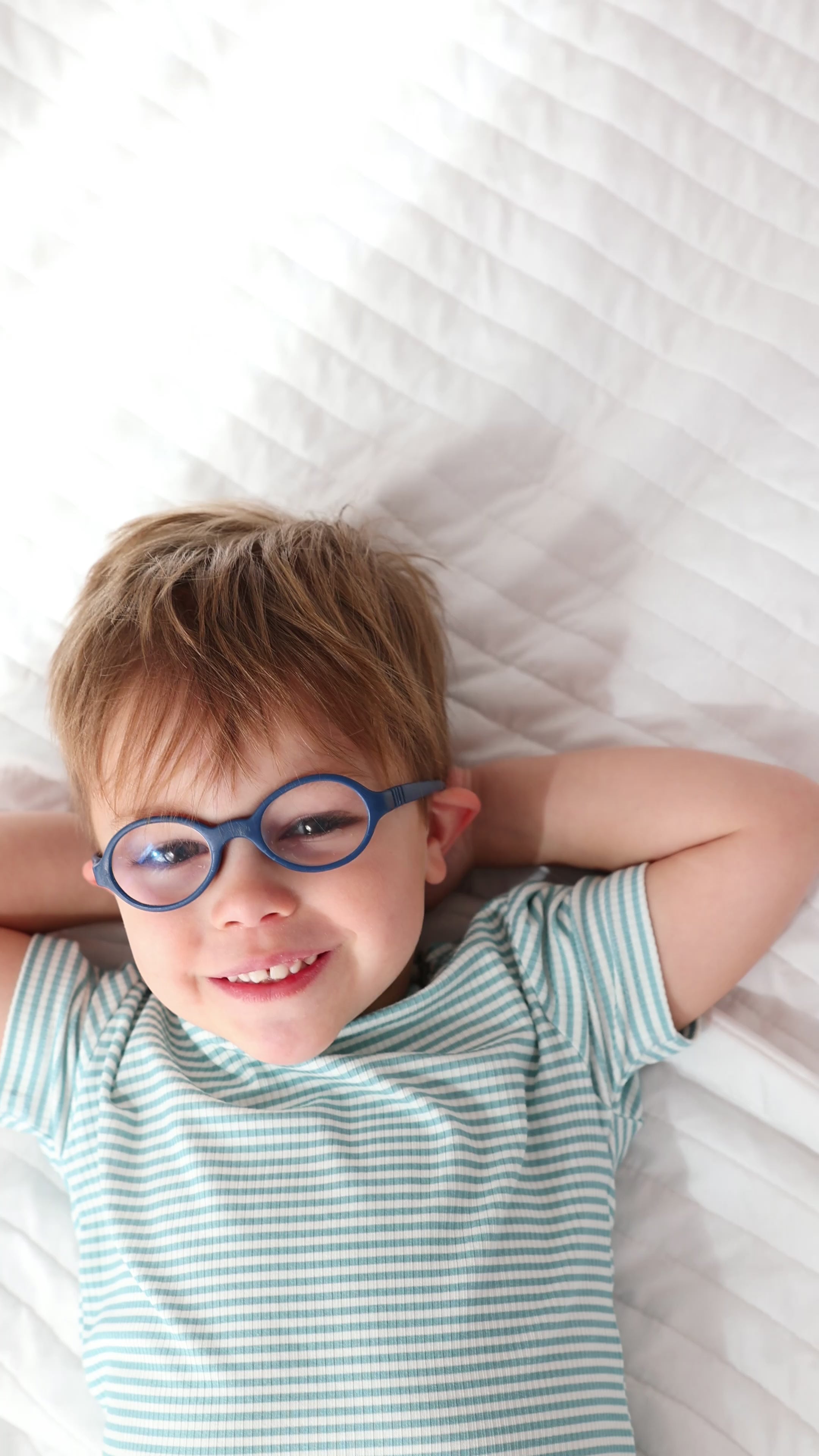 Video of a child lying on a bed wearing a blue and white striped pajama set