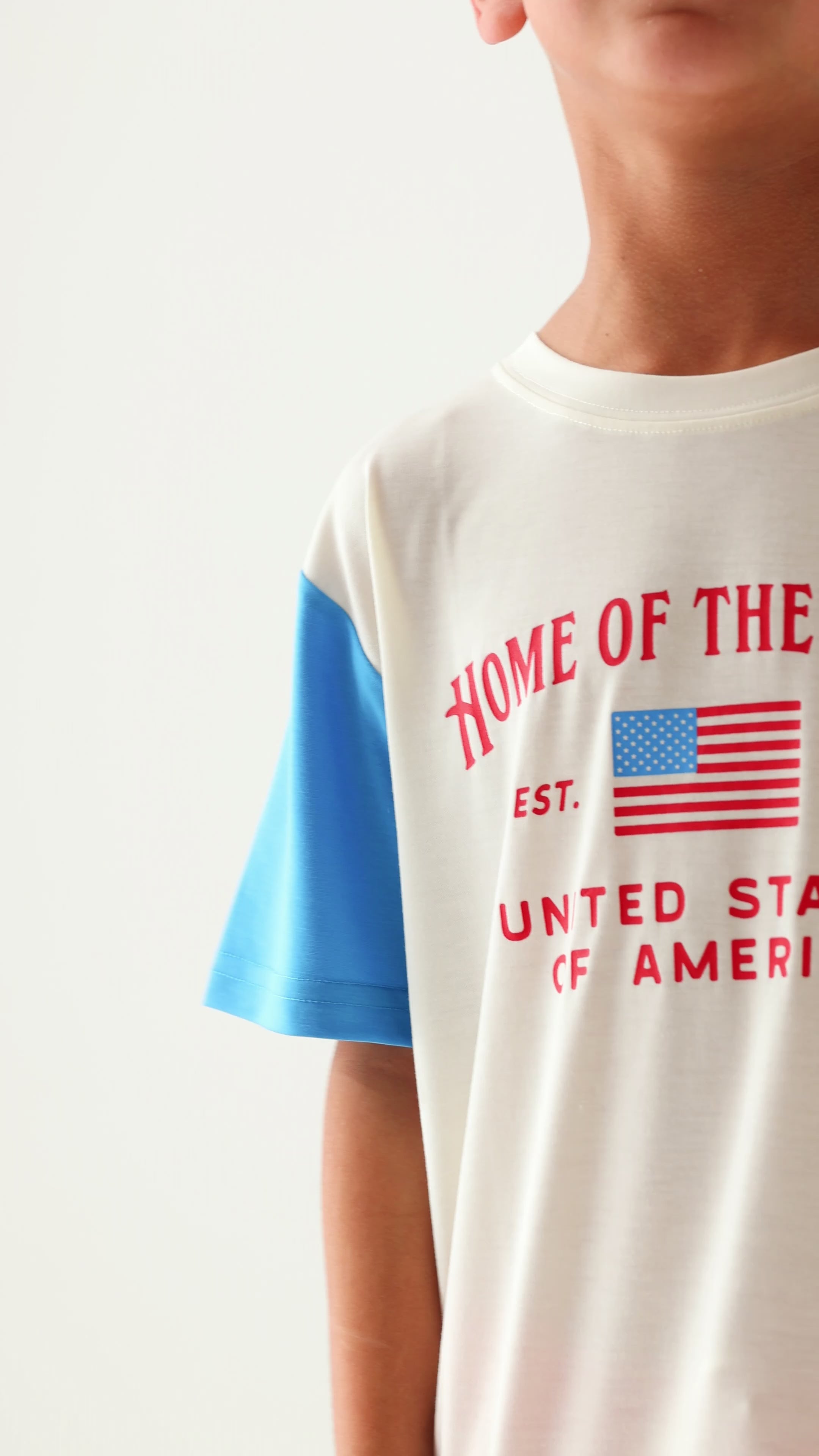 Child wearing a 'Home of the Brave' t-shirt with blue sleeves on a white background
