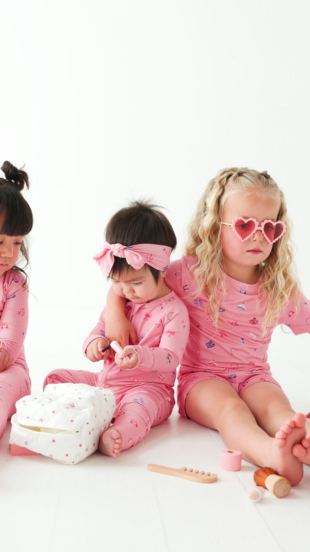 Video of three children in pink pajamas sitting on a white surface with toys around them.