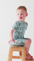 Child wearing a blue short romper with summer patterns sitting on a stool