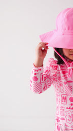 Child wearing a pink and white patterned long sleeve one-piece swimsuit and a matching light pink sun hat on a white background
