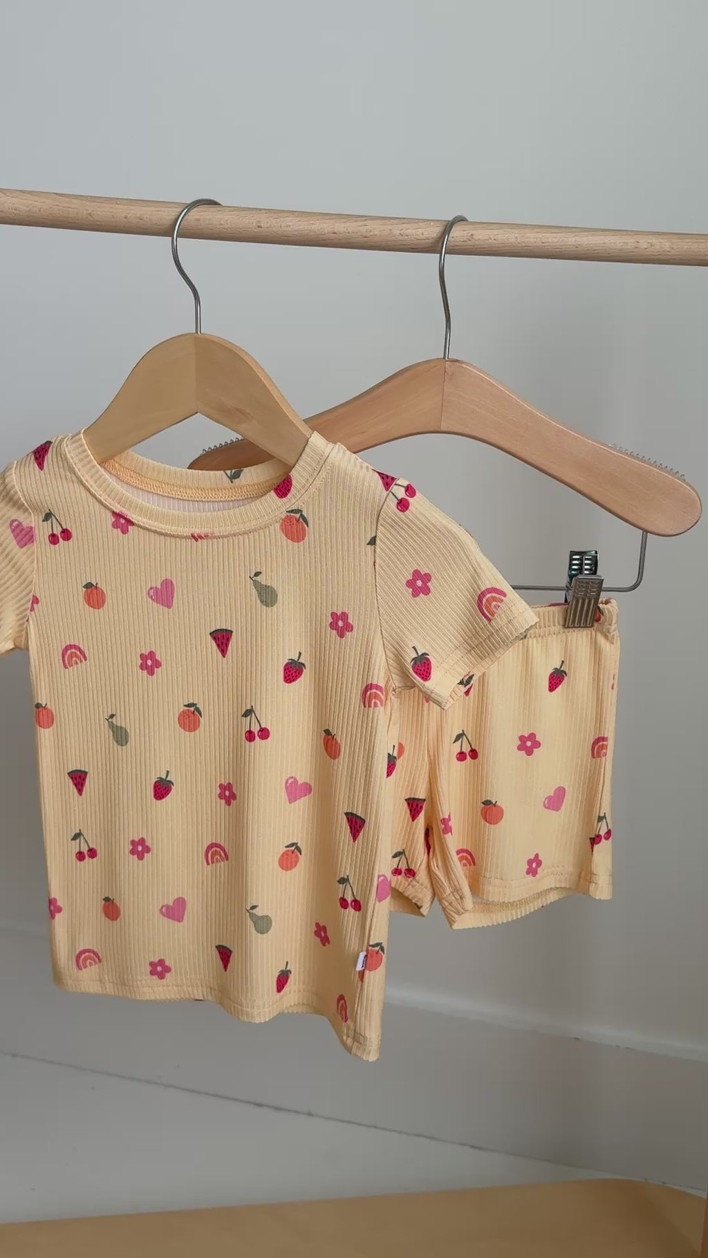 Yellow shorts pajama set with fruit and heart patterns hanging on a rack