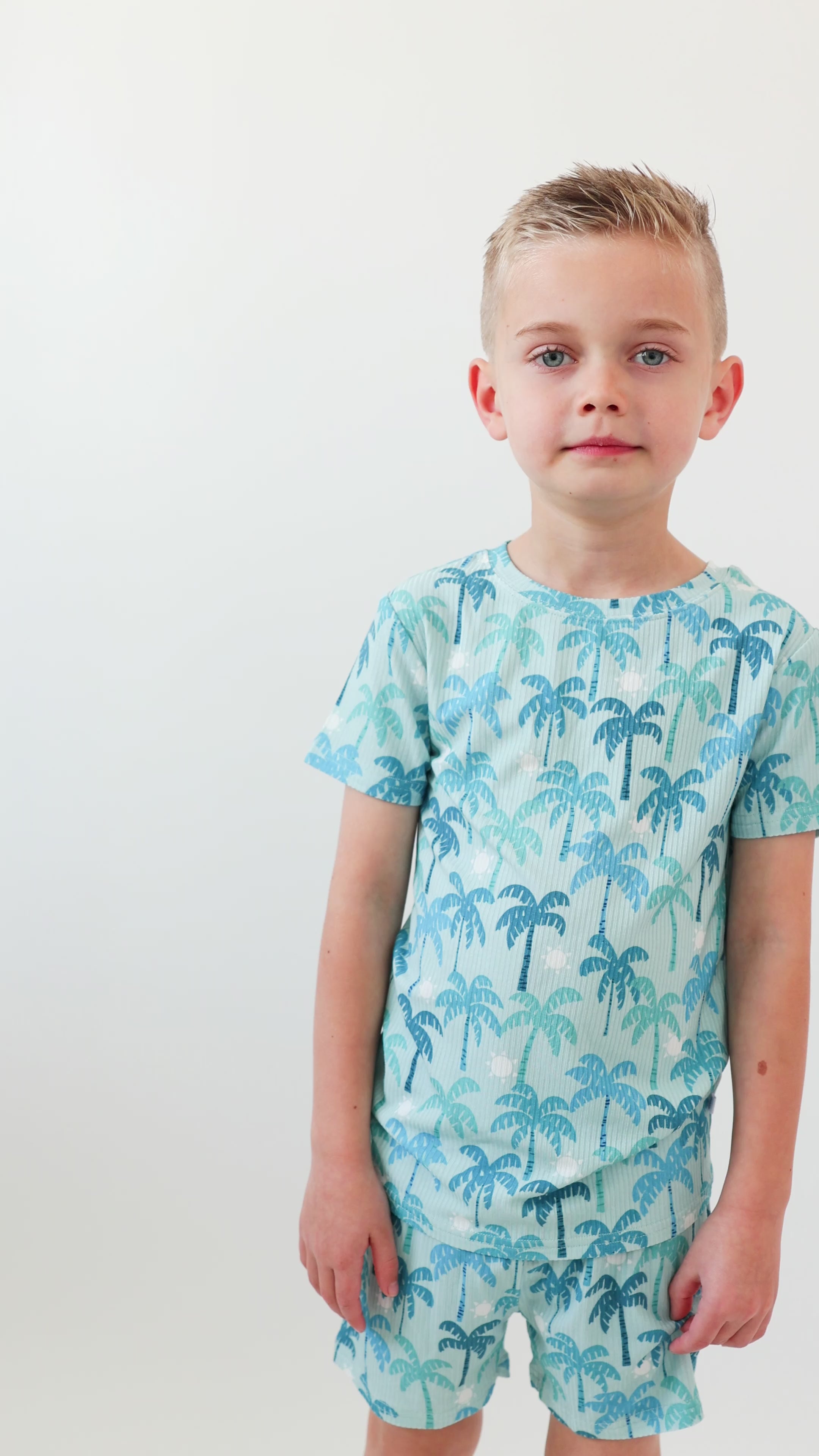 Child wearing a blue palm tree patterned pajama on a white background