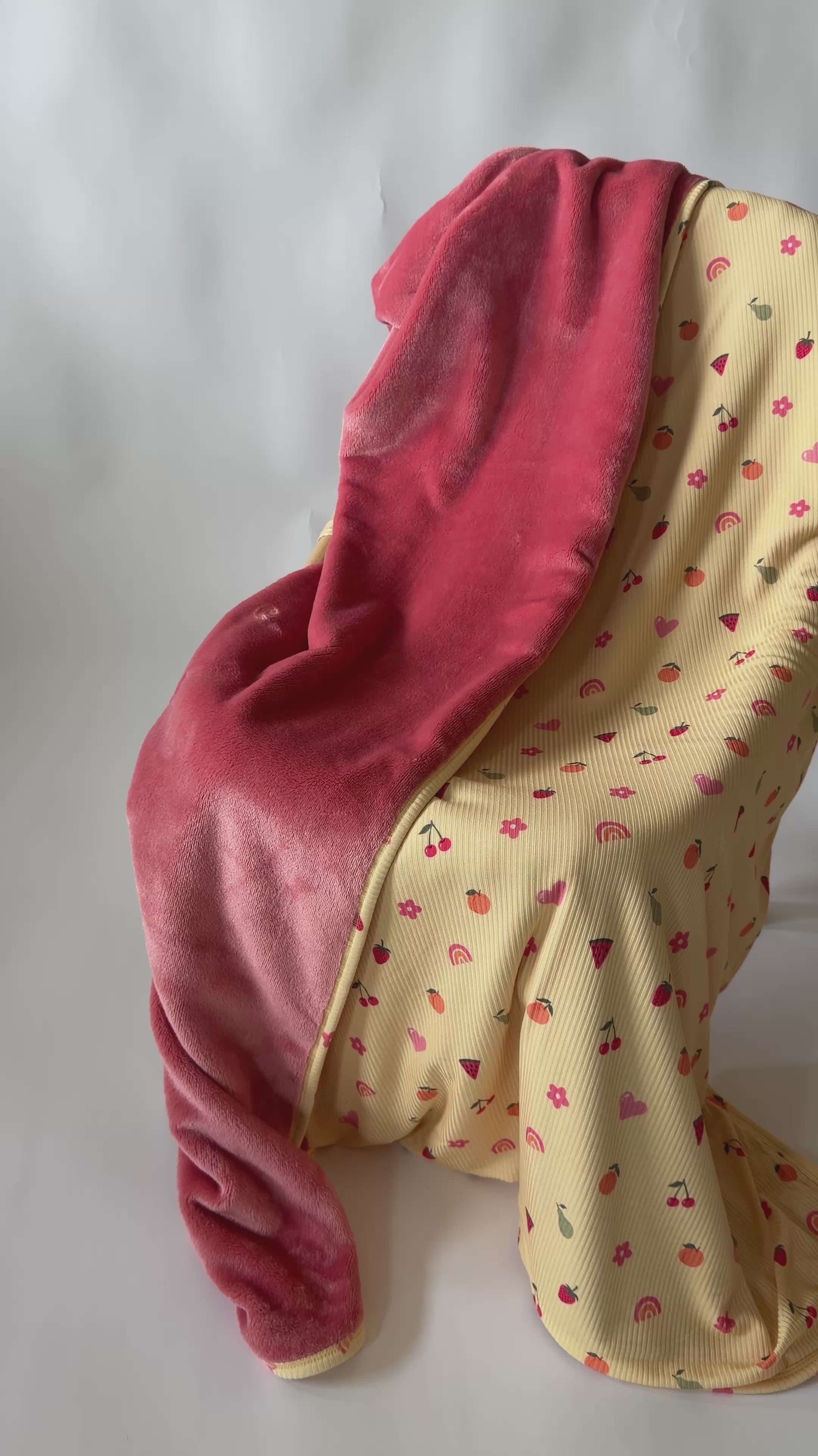 Baby blanket with colorful fruit pattern on one side and solid color on the other draped over a chair