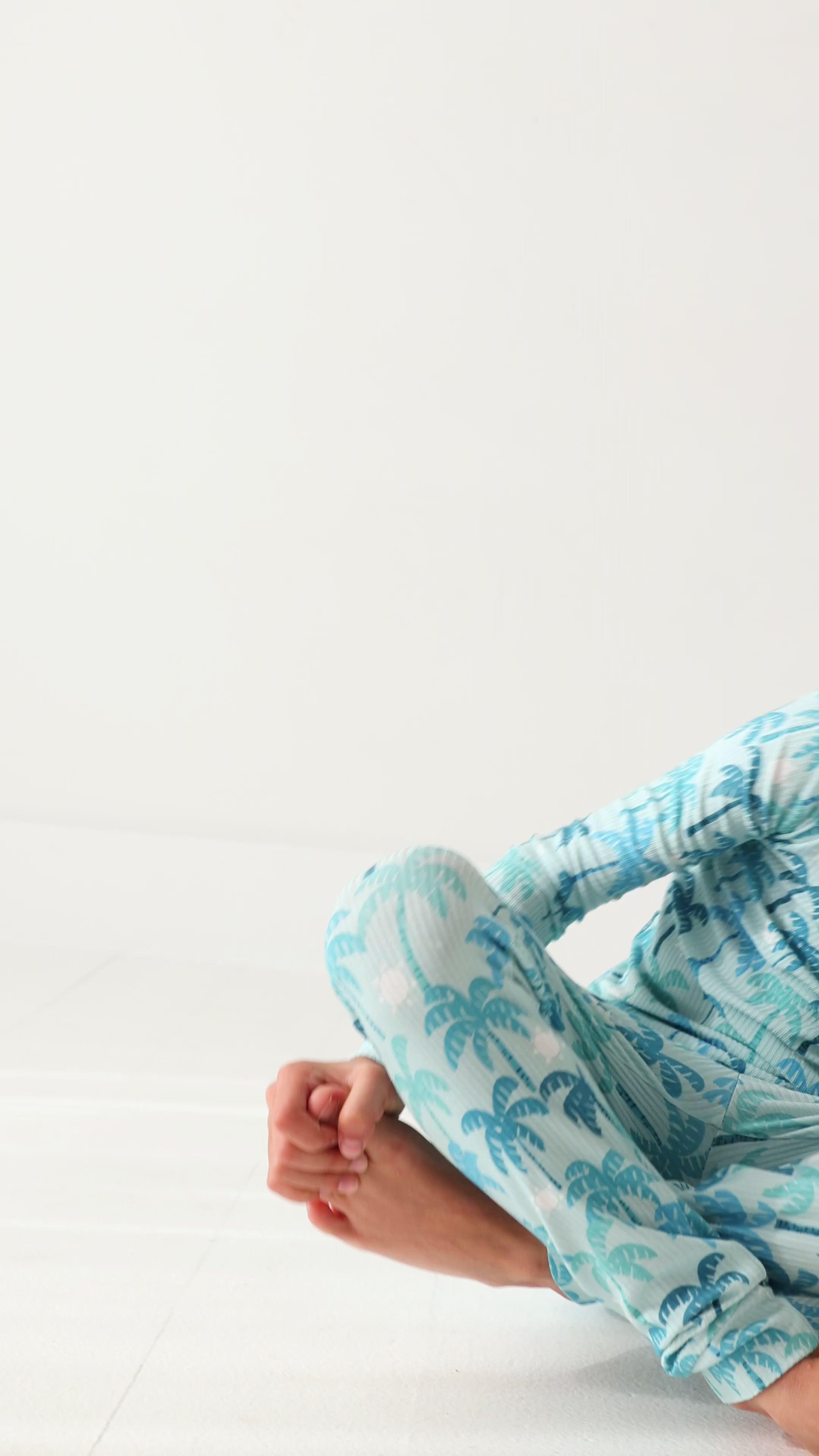 Child wearing a blue palm tree patterned pajama set on a white background.