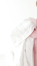 Child wearing a pink striped long sleeve pajama set holding a blanket on a white background