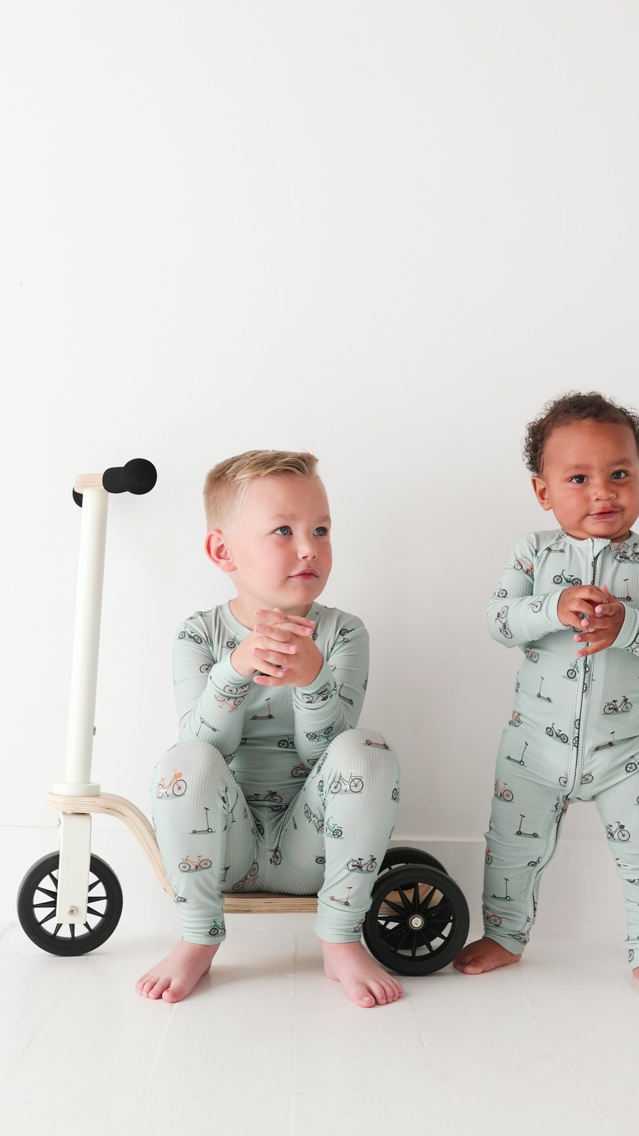 Video of two children wearing matching pajamas standing next to a small bike on a white background
