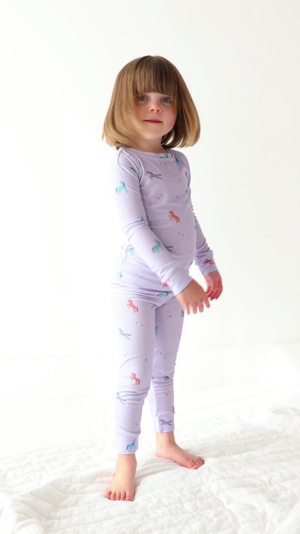 Video of a child wearing a purple pajama set with unicorn prints on a white background