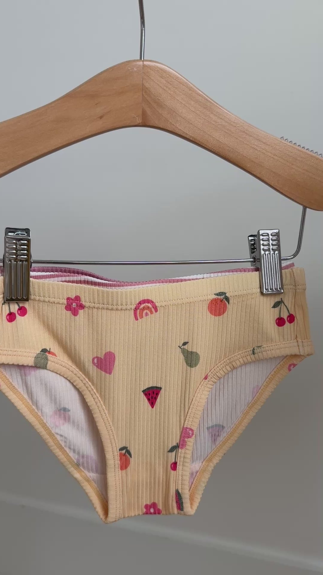 Set of three children's underwear with floral, girly, and striped patterns hanging on a rack