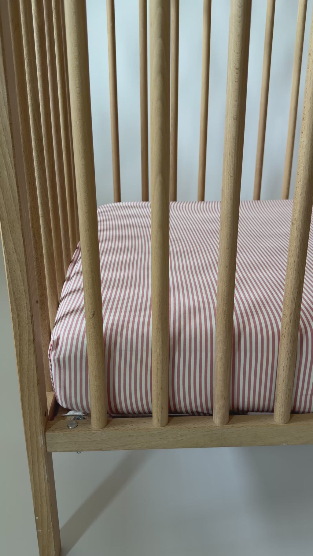 Wooden crib with pink striped sheet on a white background