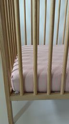Wooden crib with pink striped sheet on a white background