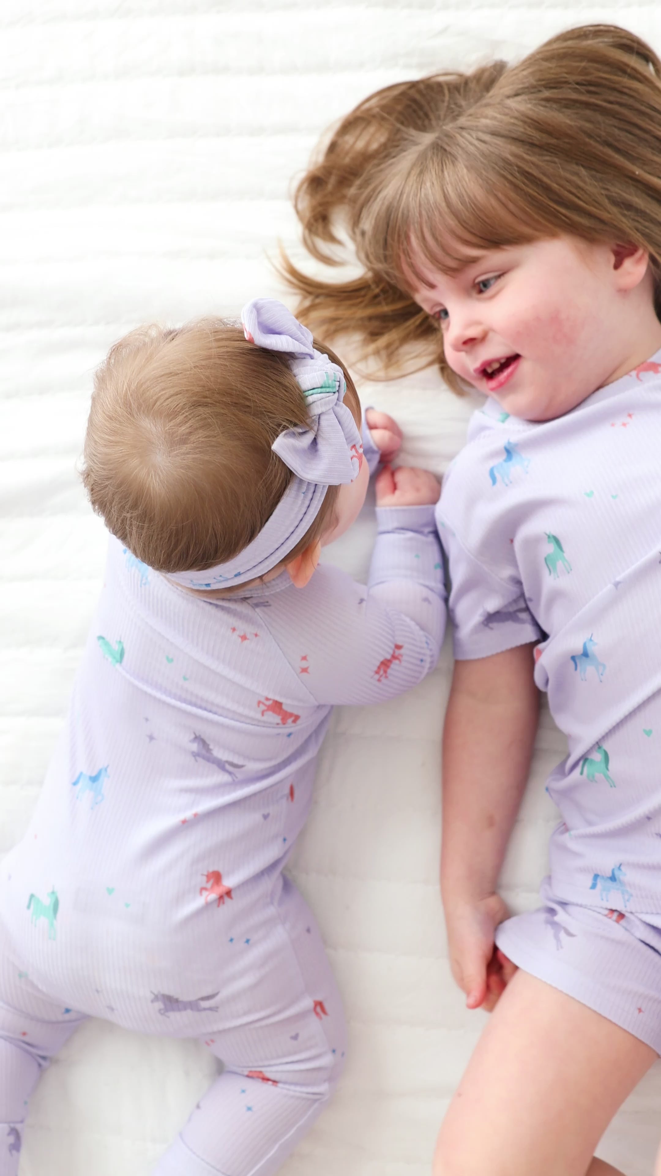 Video of two children in matching pajamas lying on a white bed.