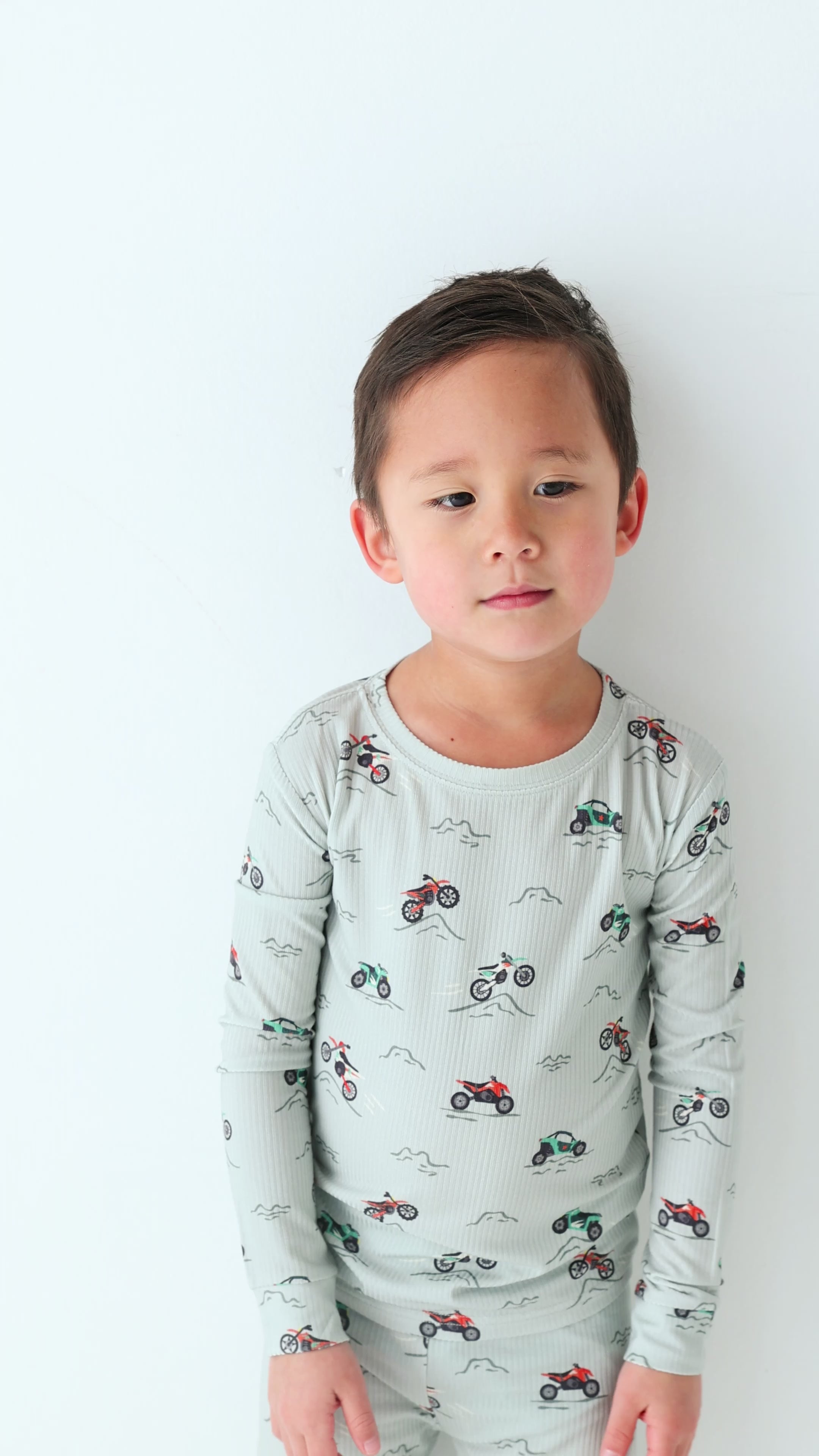 Child wearing a long sleeve pajama set with vehicle patterns on a white background