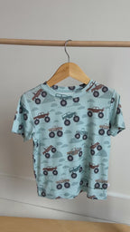 Children's light blue t-shirt with monster truck pattern hanging on a rack