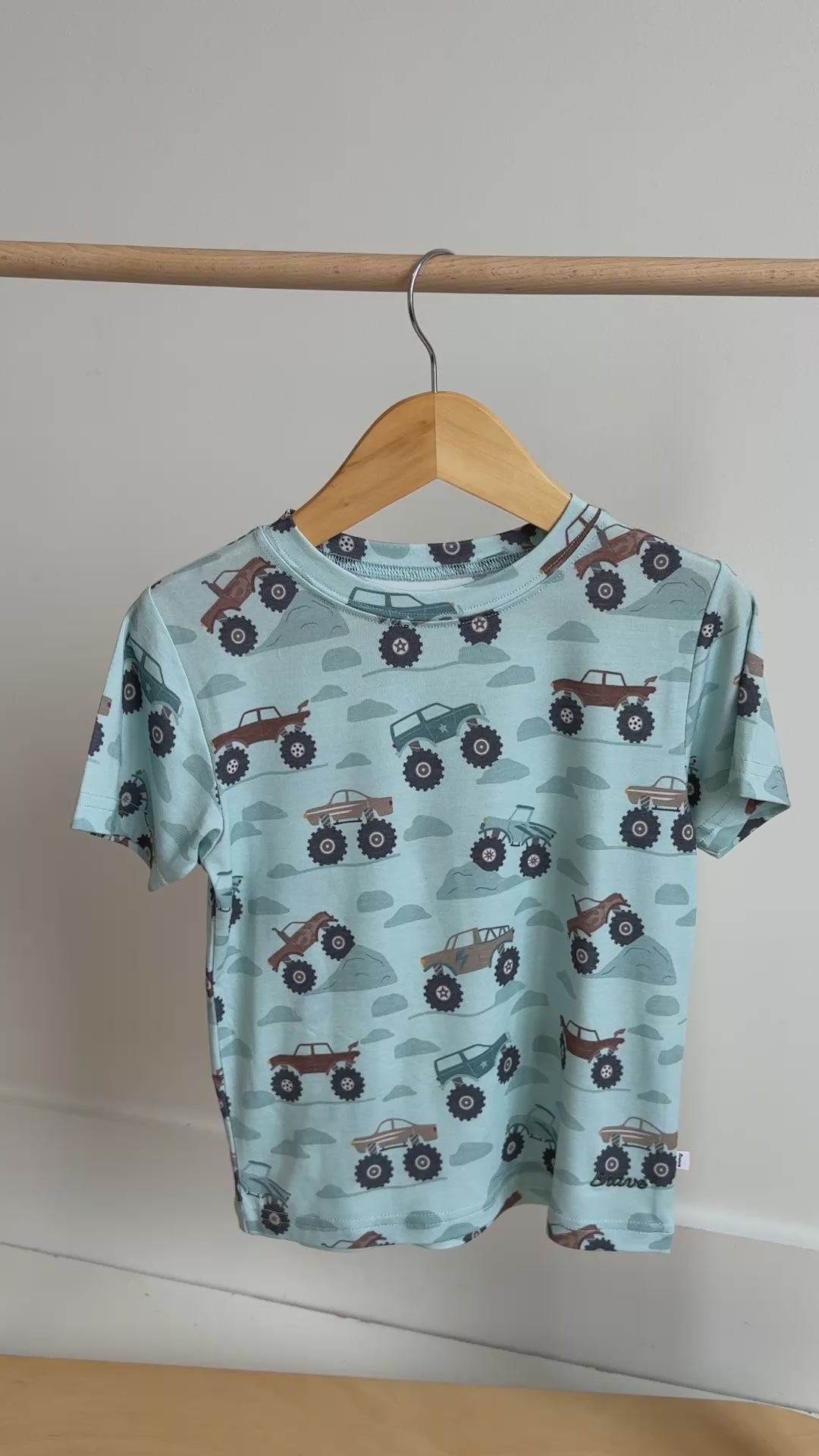 Children's light blue t-shirt with monster truck pattern hanging on a rack