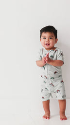 Baby wearing a light gray onesie with vehicle patterns on a white background