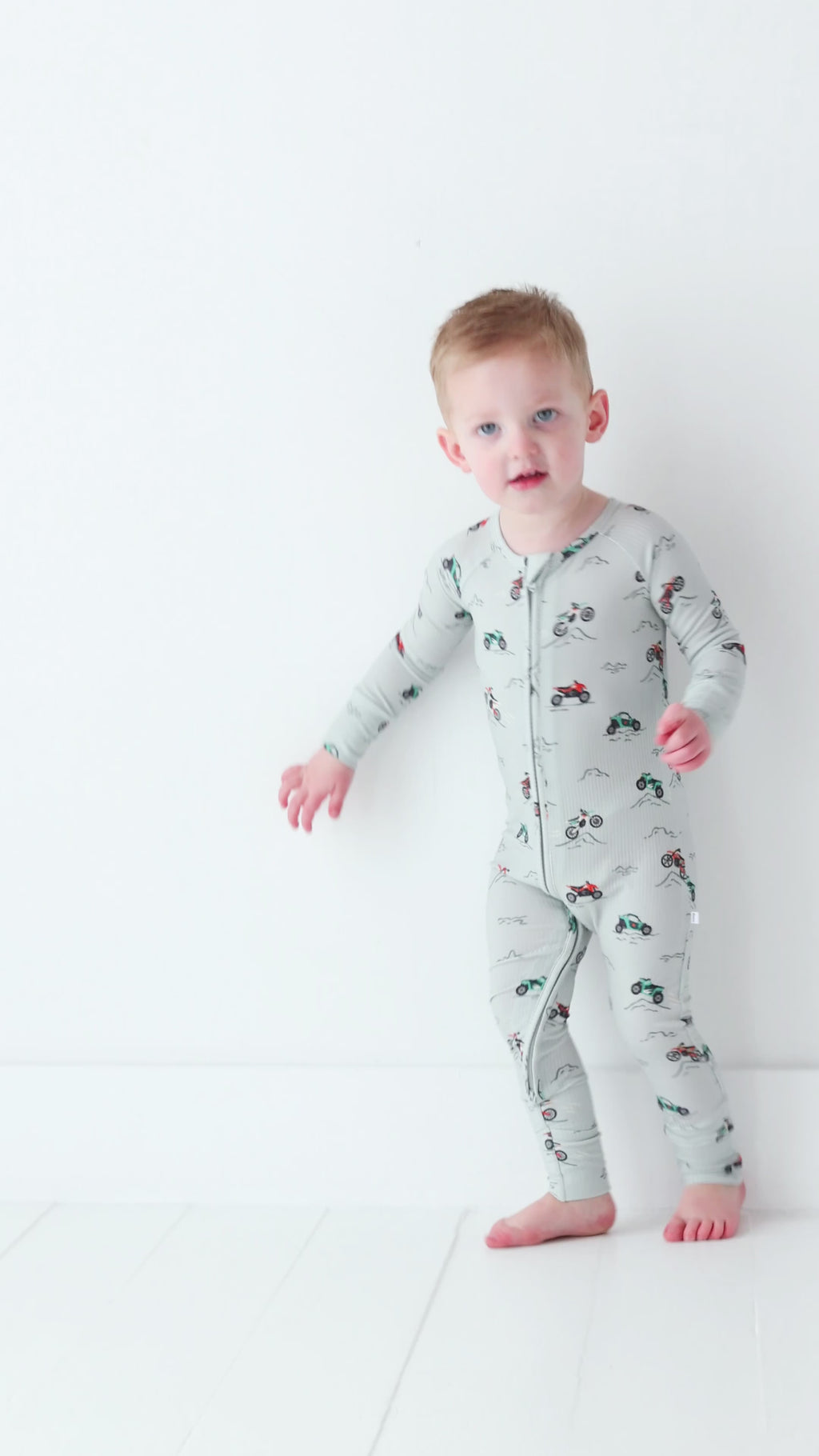 Child wearing a long-sleeve onesie with vehicle patterns on a white background