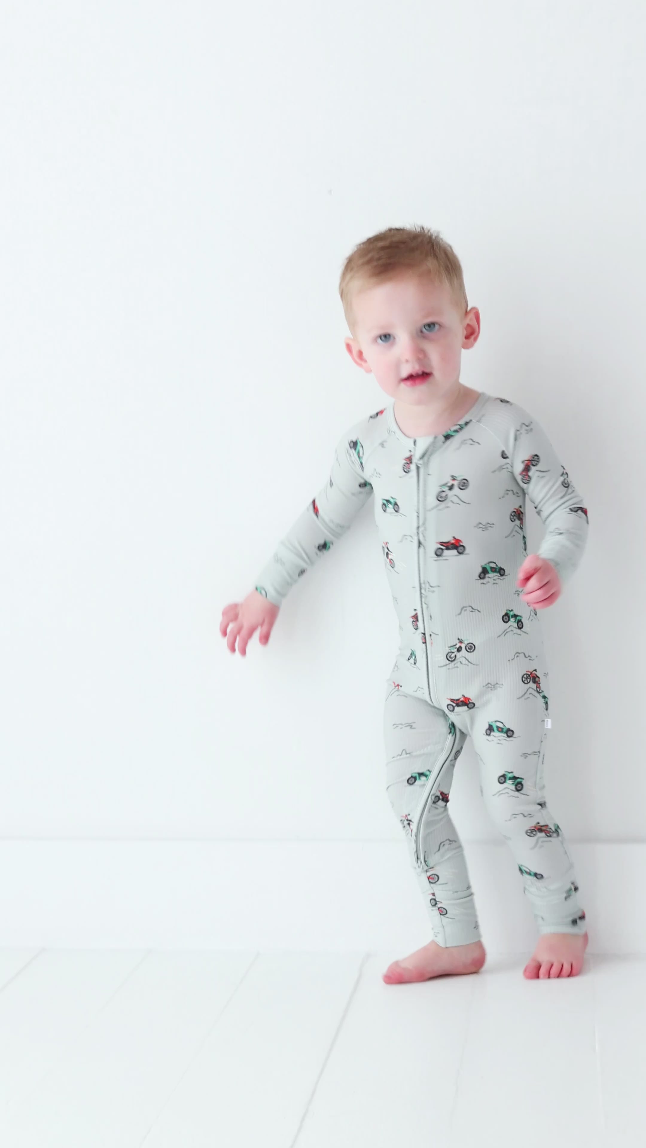 Child wearing a long-sleeve onesie with vehicle patterns on a white background