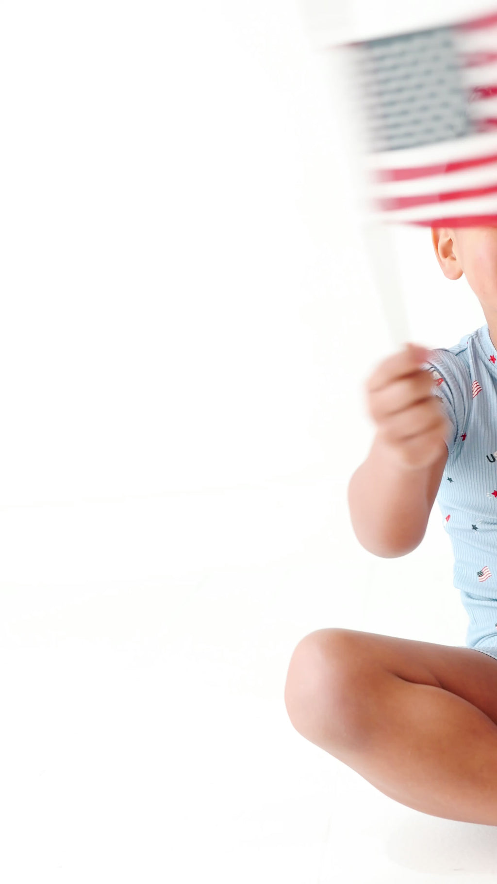 Child wearing a light blue outfit with small American flag pattern, holding a miniature American flag.