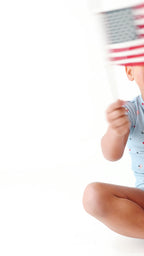Child wearing a light blue outfit with small American flag pattern, holding a miniature American flag.