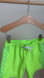 Green swim shorts with checkered side panels hanging on a rack