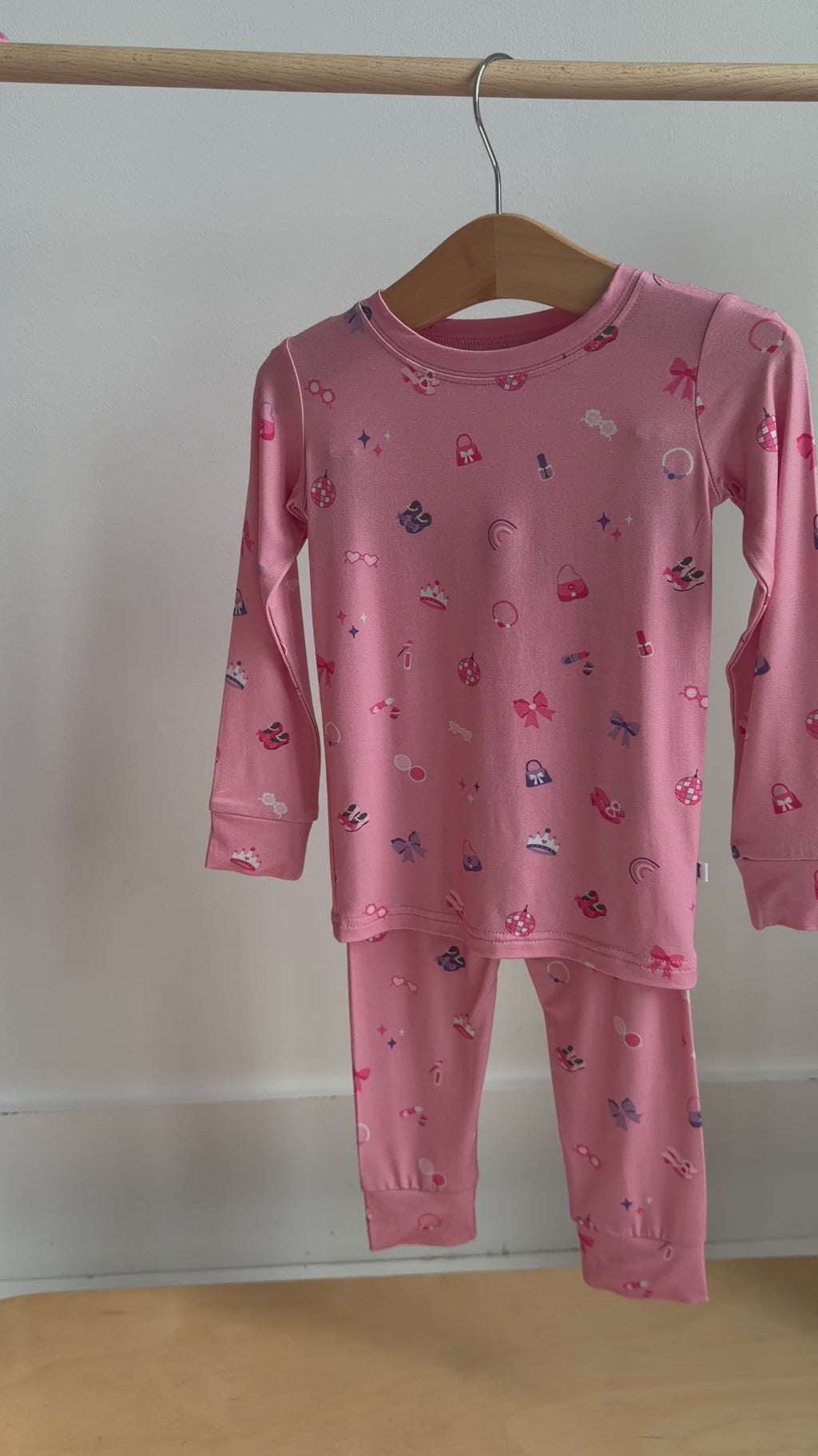 Video of a pink children's pajama set with a girly pattern hanging on a rack
