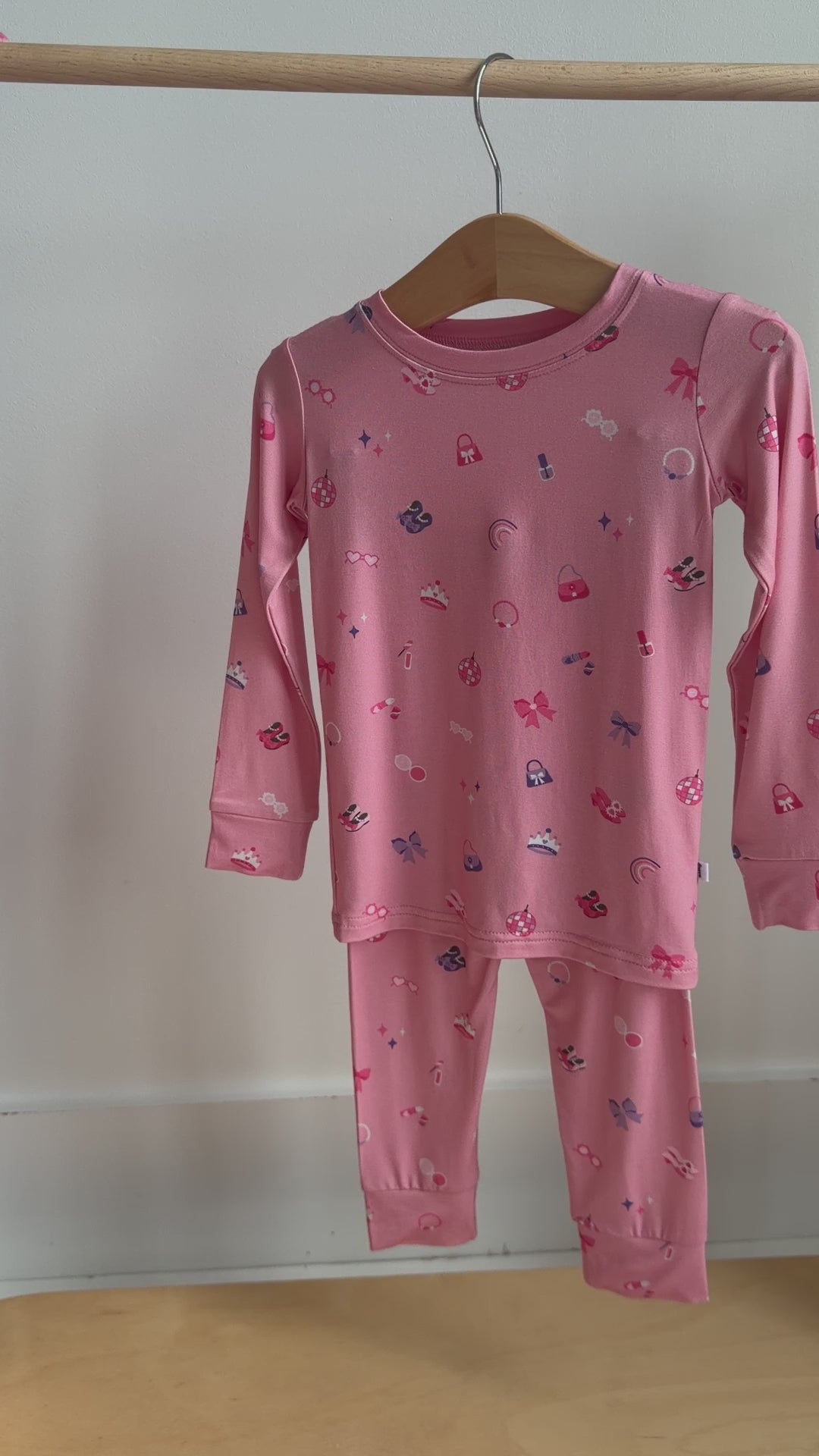 Video of a pink children's pajama set with a girly pattern hanging on a rack