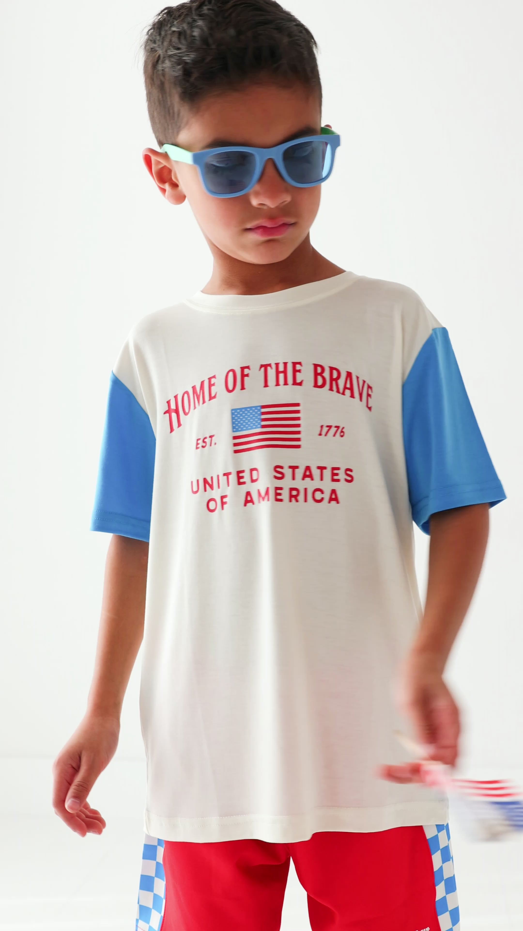 Child wearing a white t-shirt with blue sleeves and red shorts on a white background