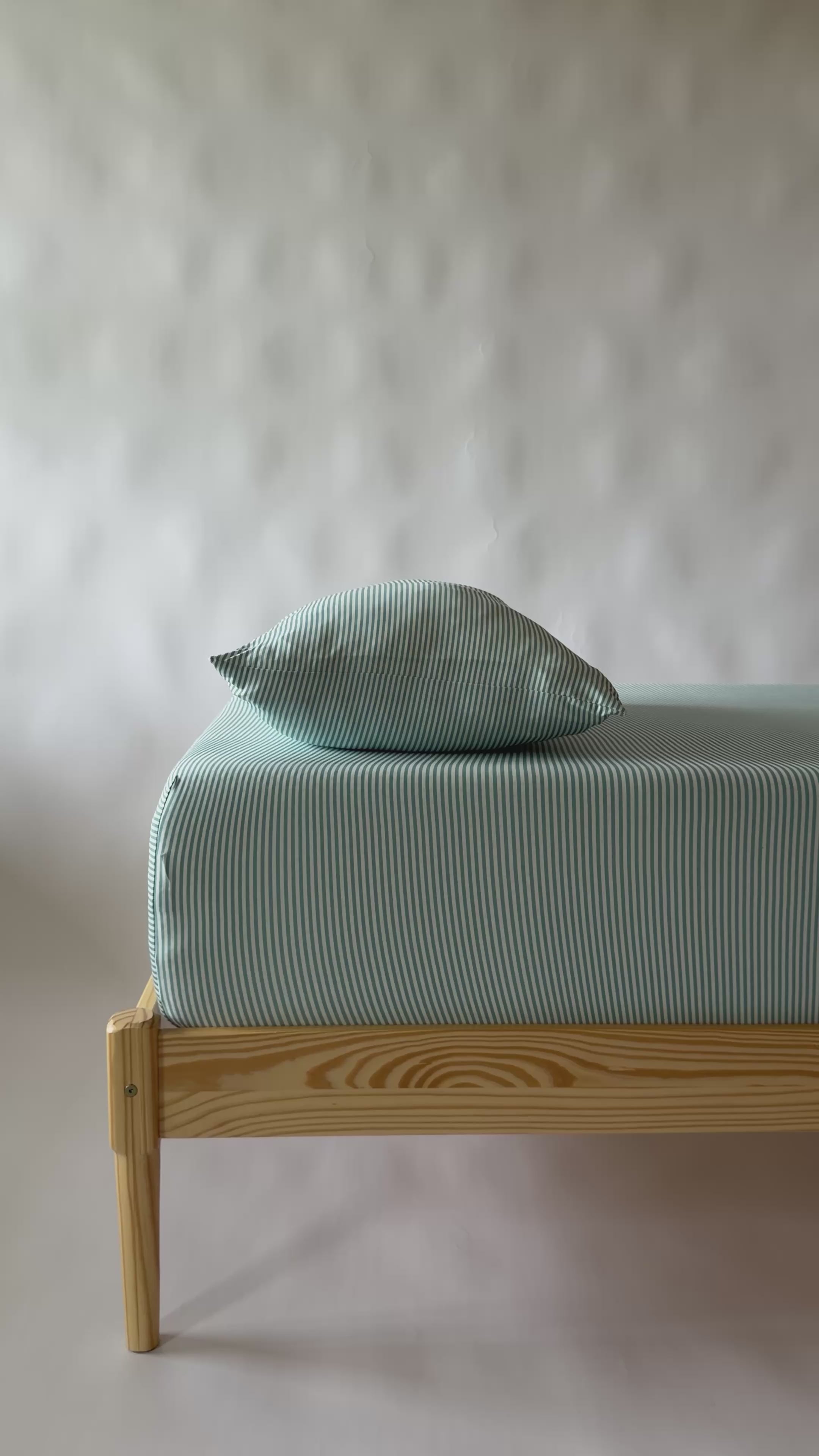 Video of a bed with light blue striped bedding and a wooden frame on a white background