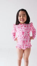 Child wearing a pink and white patterned long sleeve one-piece swimsuit on a white background