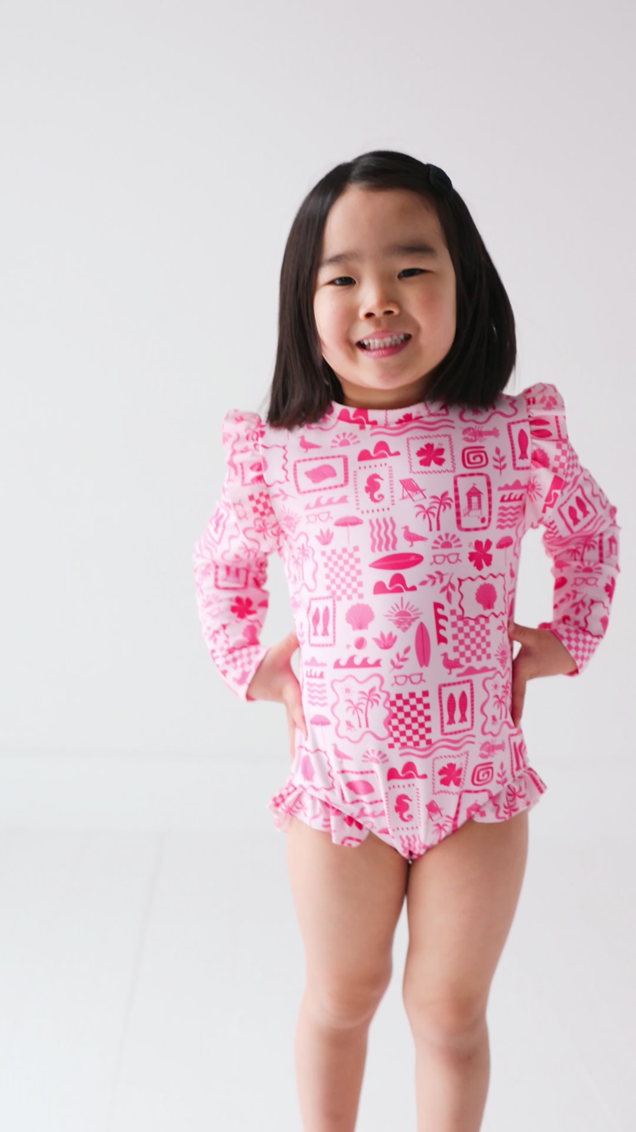 Child wearing a pink and white patterned long sleeve one-piece swimsuit on a white background
