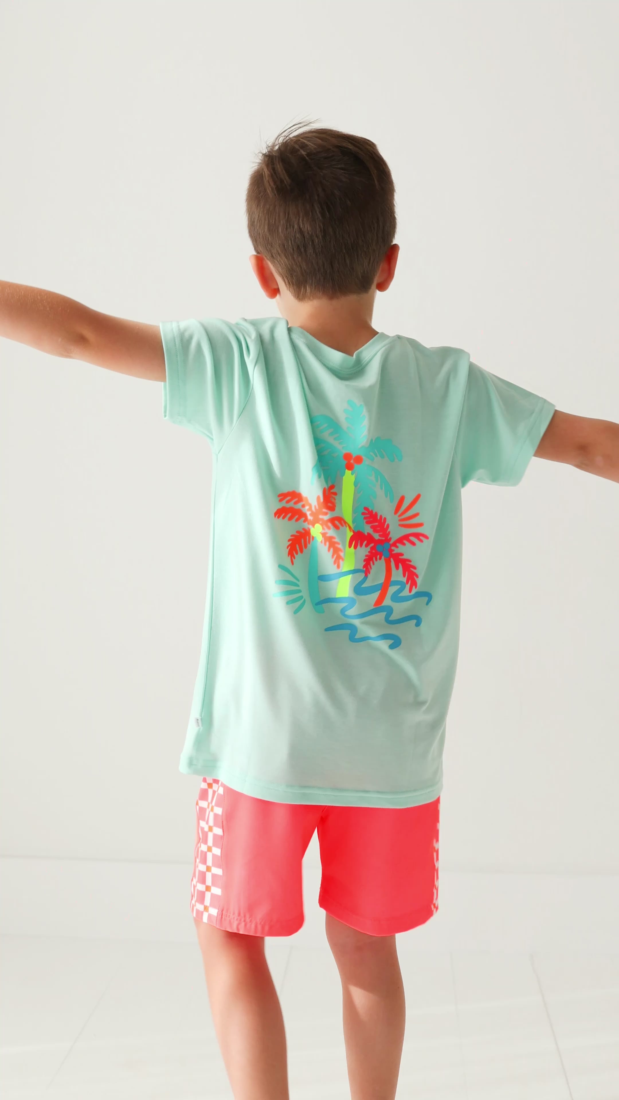 Child wearing a light blue t-shirt with colorful palm tree design on a white background